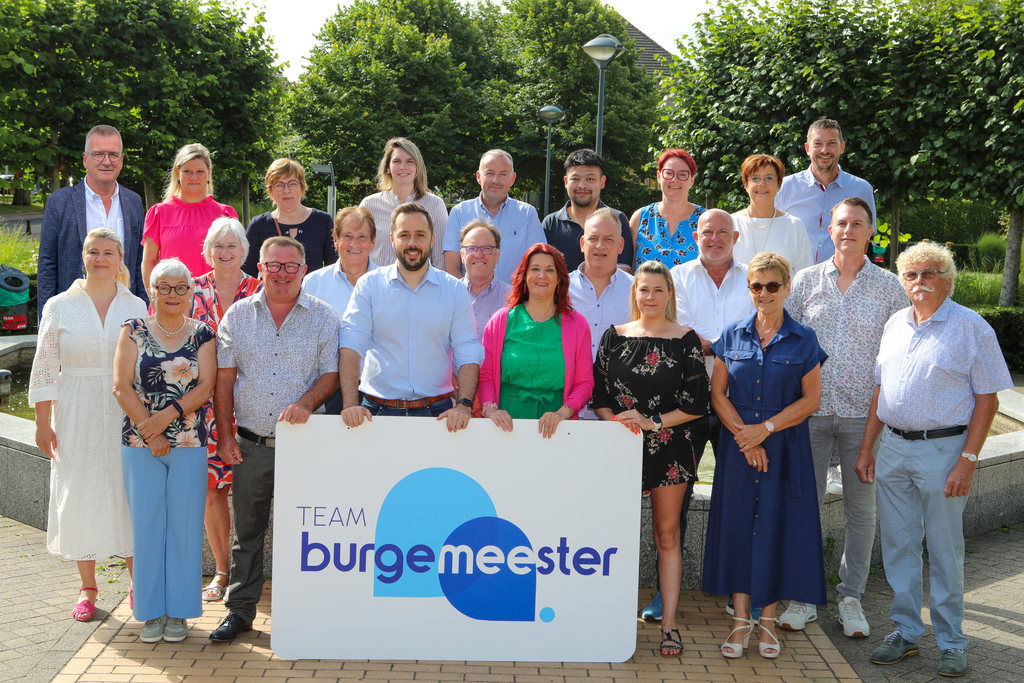 Groepsfoto van het team van Team Burgemeester met een groot bord met het logo